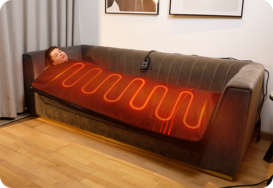 Person lying on a heated massage sofa in a room with light-colored walls and wooden floor.