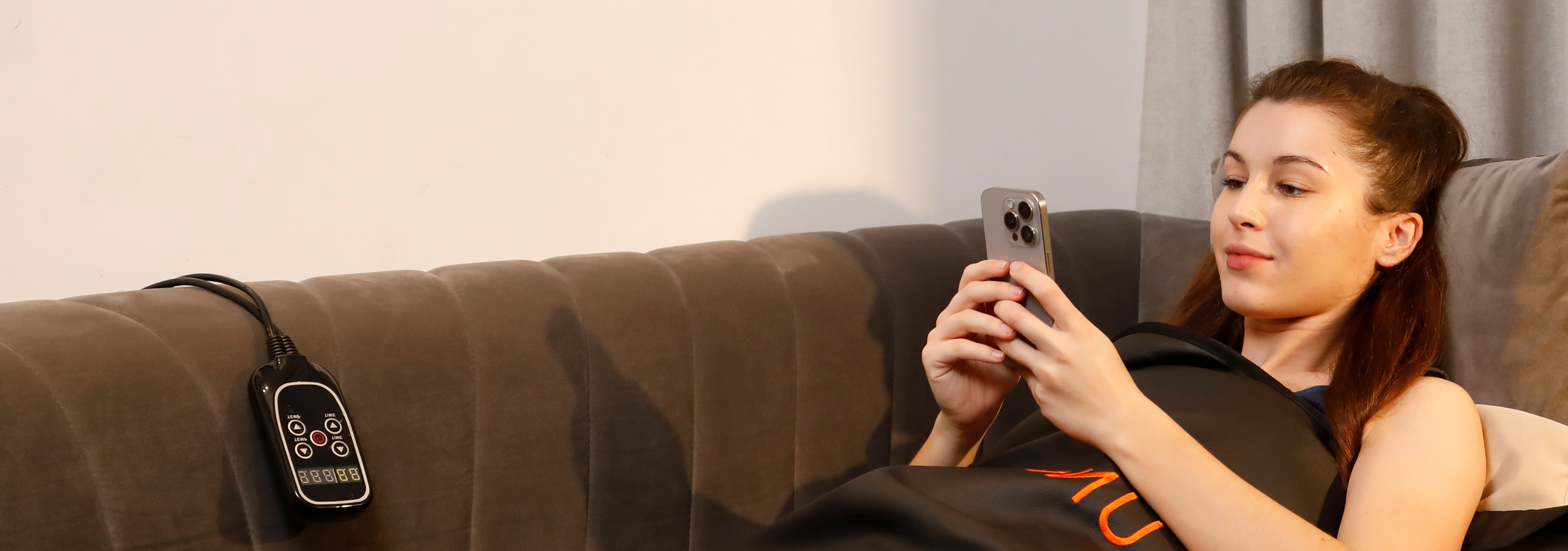 A woman uses her phone during an infrared sauna blanket treatment
